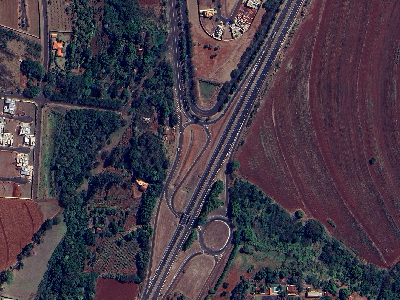 Aqui há uma foto aérea distante da parte de uma interseção em 'Y' na faixa esquerda e uma rotatória circular do lado direito, localizada no Brasil.