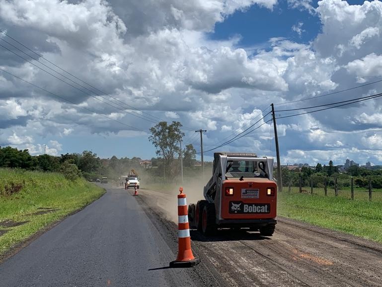 Aqui encontra-se uma foto de obra rodoviária na etapa de pavimentação. No centro direito da imagem há uma máquina bóbiquete de proporção pequena realizando o nivelamento da camada de pedras.